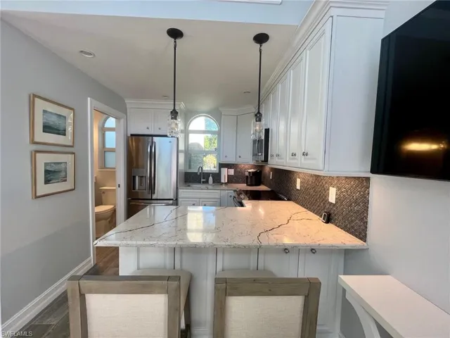 Kitchen with light stone counters, stainless steel appliances, white cabinets, a peninsula, and pendant lighting