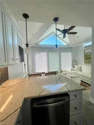 Kitchen with light stone countertops, dishwasher, pendant lighting, a peninsula, and lofted ceiling