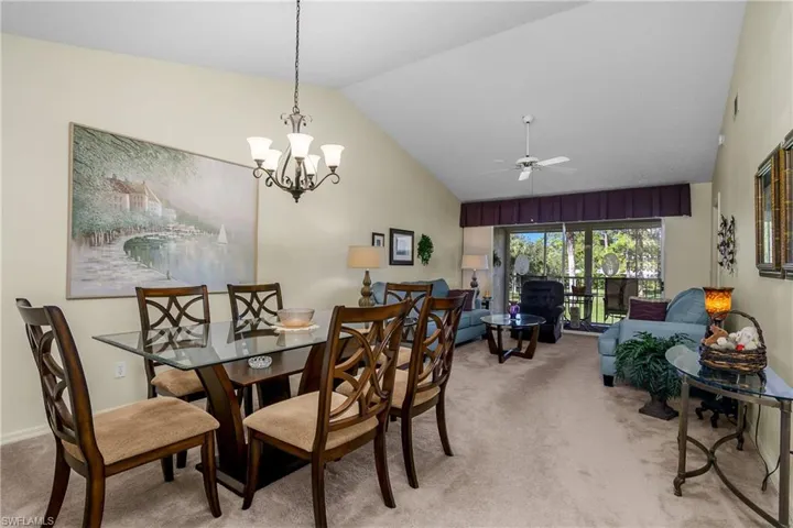 Dining room with light carpet, lofted ceiling, a ceiling fan, and a chandelier