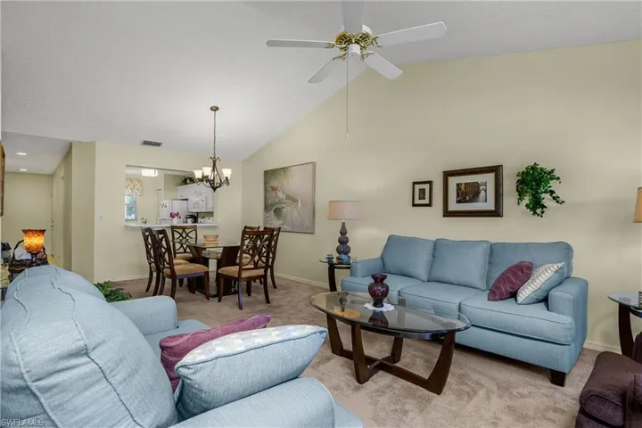 Carpeted living room featuring high vaulted ceiling, a chandelier, ceiling fan, and a textured ceiling