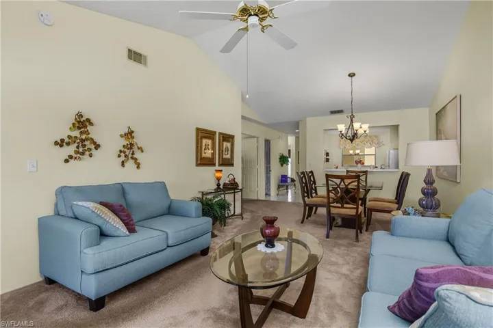 Living room with carpet flooring, ceiling fan, high vaulted ceiling, and a chandelier