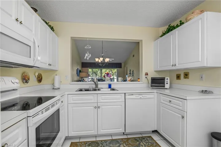 Kitchen featuring white appliances, white cabinetry, a chandelier, light countertops, and a textured ceiling