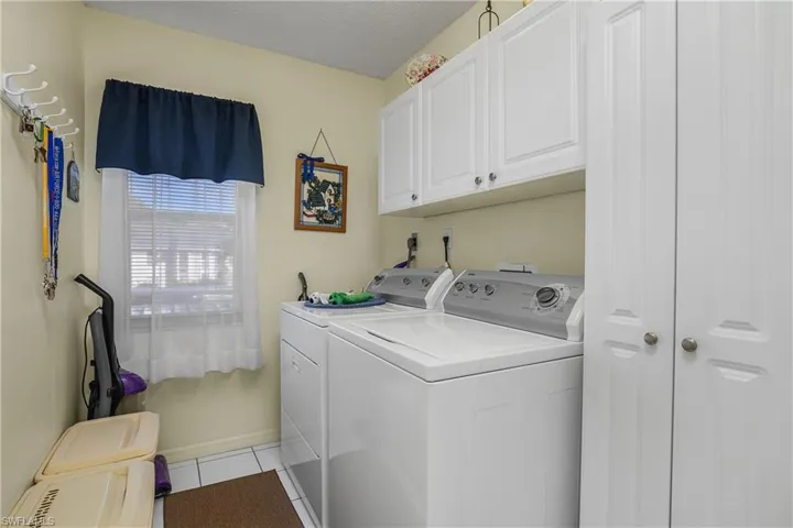 Washroom with washing machine and dryer, light tile patterned floors, cabinet space, and a textured ceiling