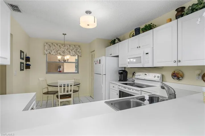 Kitchen featuring white appliances, white cabinets, light countertops, pendant lighting, and a textured ceiling