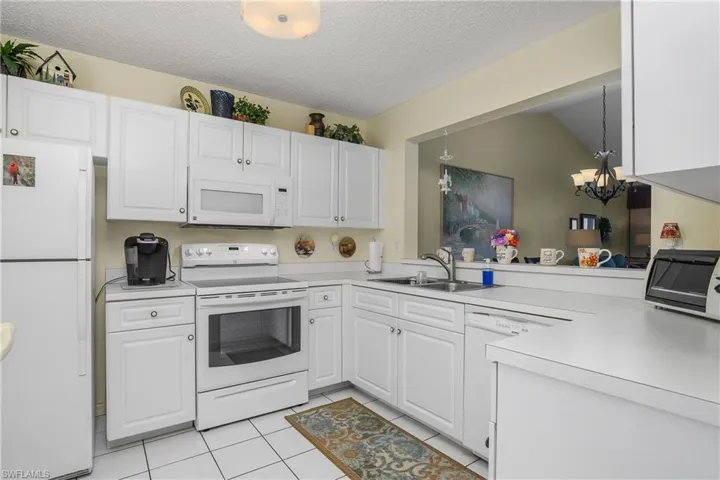 Kitchen featuring white appliances, white cabinets, a textured ceiling, light countertops, and light tile patterned flooring