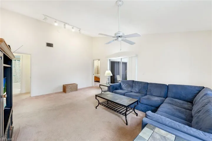 Carpeted living room featuring high vaulted ceiling, ceiling fan, and rail lighting