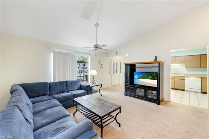 Carpeted living room featuring ceiling fan, sink, and high vaulted ceiling