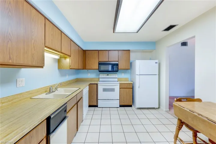Kitchen with sink, white appliances, and light tile patterned flooring