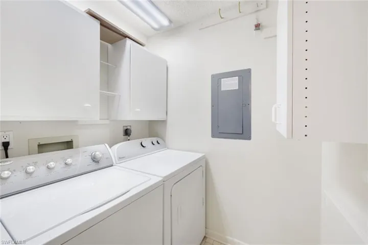 Clothes washing area featuring electric panel, cabinets, a textured ceiling, and washing machine and clothes dryer