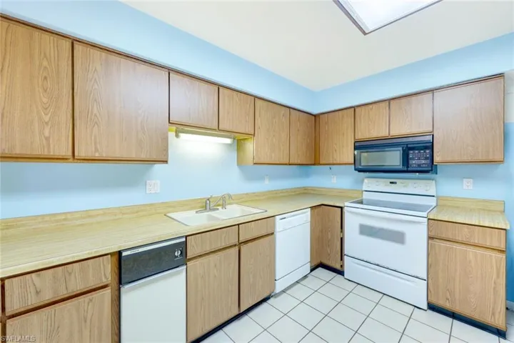 Kitchen featuring white appliances, sink, and light tile patterned flooring