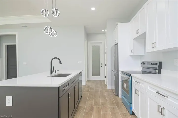 Kitchen featuring hanging light fixtures, white cabinets, sink, a center island with sink, and appliances with stainless steel finishes