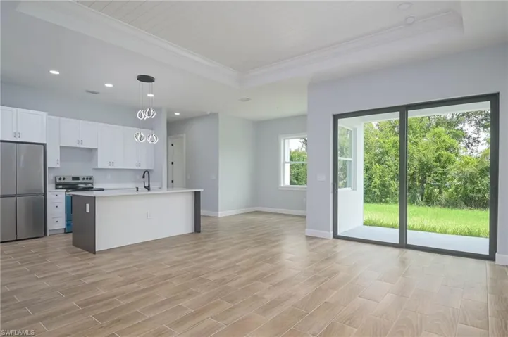 Kitchen with light wood-type flooring, an island with sink, appliances with stainless steel finishes, pendant lighting, and a raised ceiling