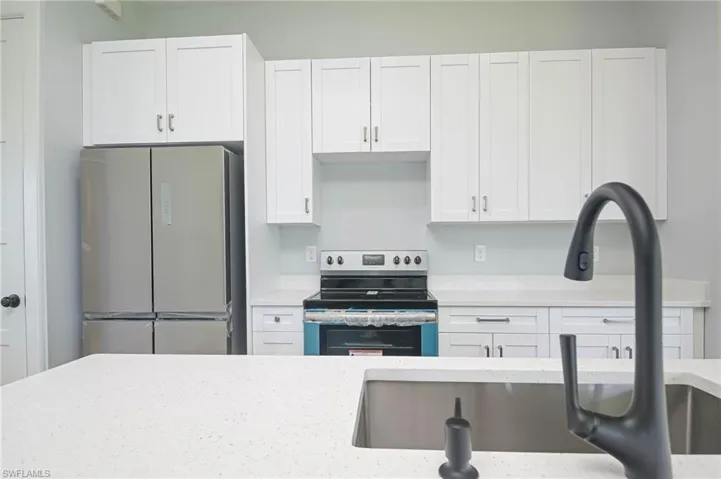 Kitchen featuring sink, white cabinets, light stone counters, and stainless steel appliances