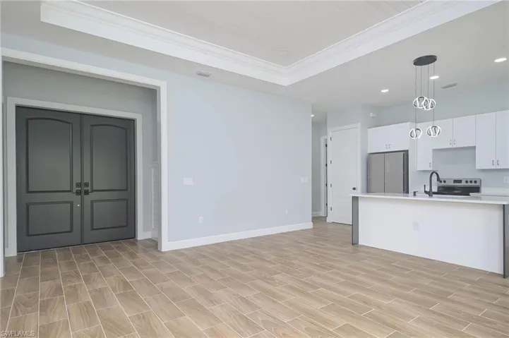 Kitchen with white cabinetry, a tray ceiling, stainless steel appliances, pendant lighting, and light wood-type flooring