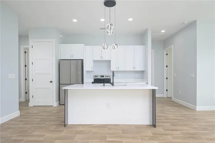 Kitchen featuring white cabinets, pendant lighting, sink, a center island with sink, and stainless steel fridge