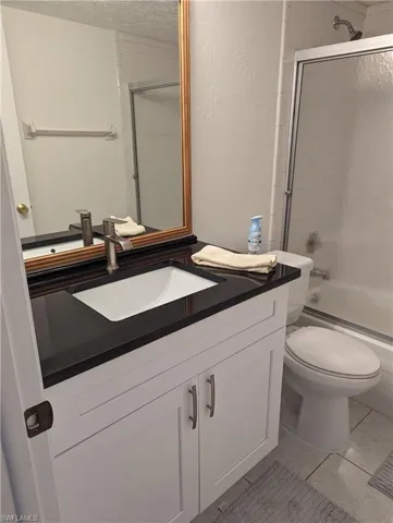 Bathroom with vanity, enclosed tub / shower combo, a textured ceiling, and light tile patterned floors
