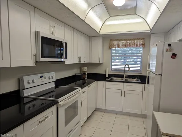 Kitchen featuring white appliances, white cabinetry, and light tile patterned flooring
