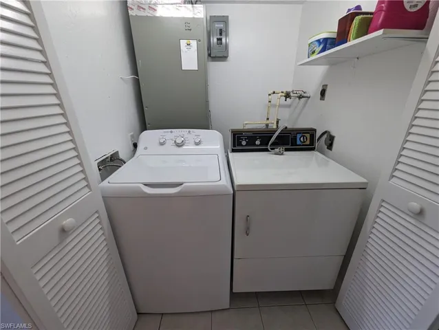 Laundry area with washing machine and clothes dryer, electric panel, and light tile patterned floors