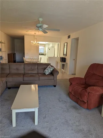 Carpeted living area featuring a textured ceiling, a chandelier, and ceiling fan
