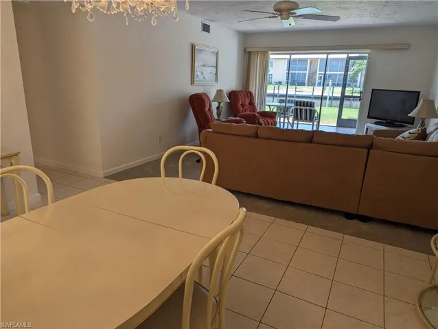 Dining space with light tile patterned flooring, a ceiling fan, a chandelier, and a textured ceiling