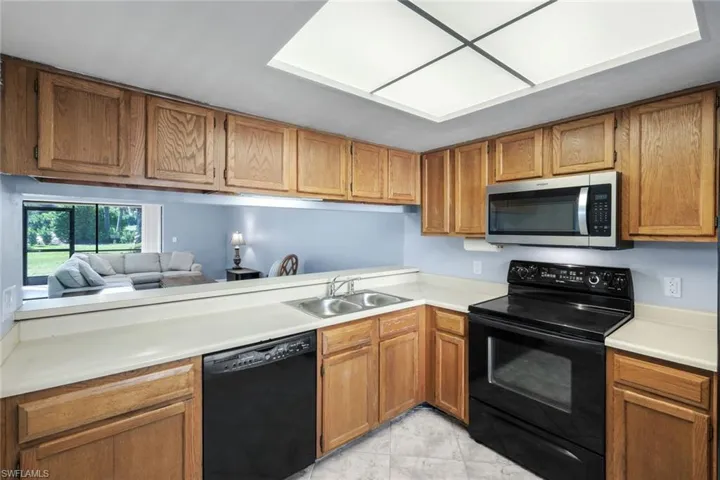 Kitchen featuring wood cabinetry, light countertops, stainless steel microwave, black electric range, and a pass-through opening to the living area