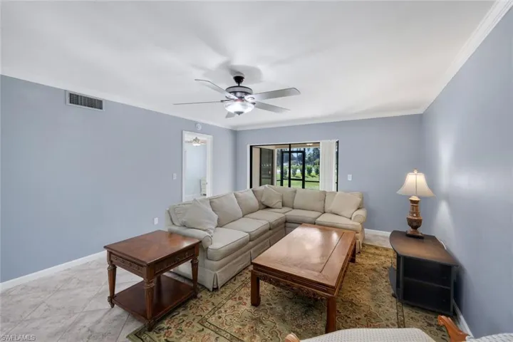 Spacious living area featuring light blue walls, a ceiling fan with integrated lighting, and crown molding