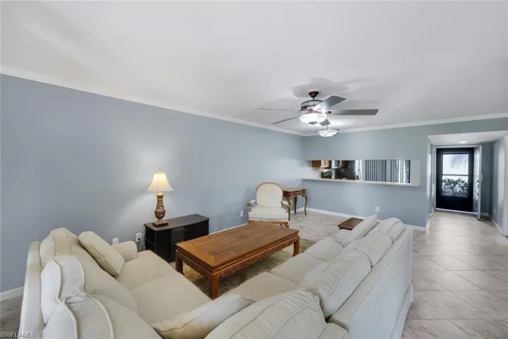 Living area featuring light blue walls with crown molding, a ceiling fan with integrated lighting, and a pass-through opening to an additional space