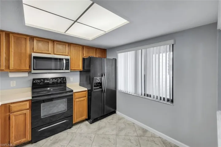 Kitchen featuring light wood cabinetry, black appliances, light-toned countertops, and tile flooring