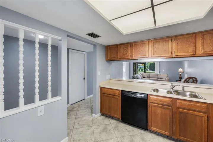 Kitchen featuring wood cabinetry, a double basin stainless steel sink, black dishwasher, and laminate countertops