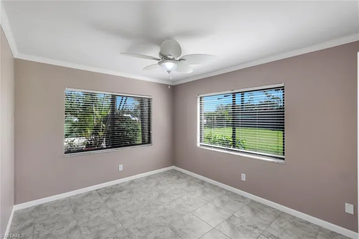 Spacious room featuring tile flooring, neutral wall tones, crown molding, and two windows equipped with blinds