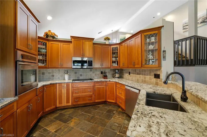 Granite counters, Stainless Steel appliance with cooktop and wall oven, chestnut wood cabinetry, tile backsplash and flooring.