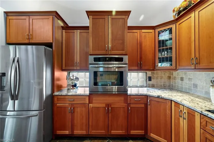 Kitchen featuring wood cabinetry, decorative backsplash, light stone countertops, a healthy amount of sunlight, and appliances with stainless steel finishes