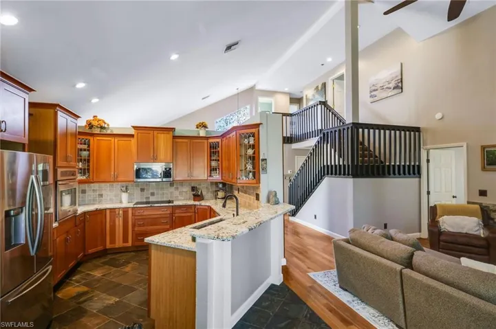 Kitchen with chestnut wood cabinetry, tile backsplash, granite stone counters, stainless steel appliances and lofted ceiling