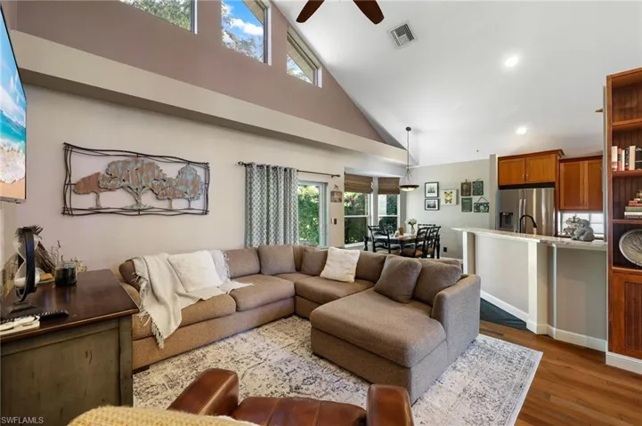 Family room with 2nd story vaulted ceiling, windows, plant shelf, ceiling fan, and wood flooring