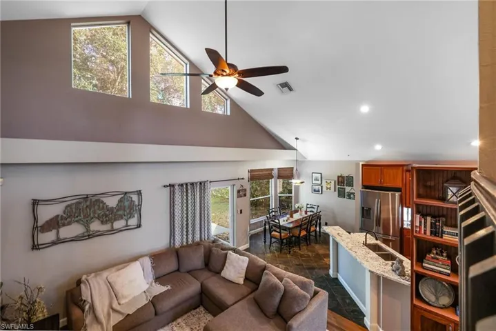 Family room view from staircase landing. Natural light with windows, ceiling fan, wood and tile flooring, plant shelf and high vaulted ceiling
