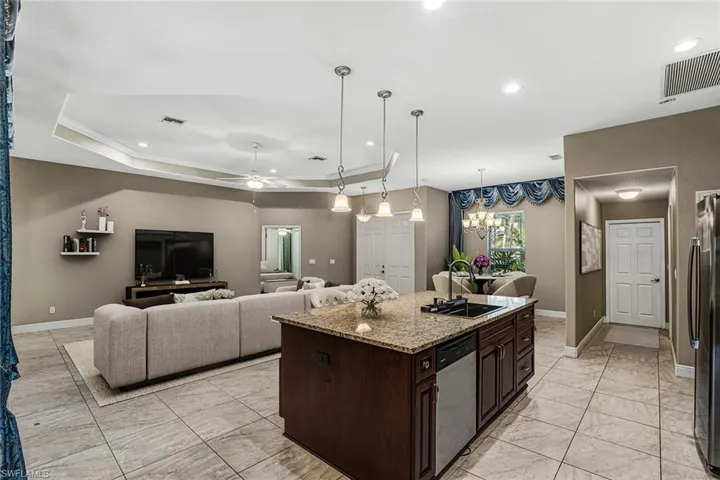 Kitchen with dark wood finish cabinetry, a ceiling fan, a center island with sink, stainless steel appliances, and light stone counters
