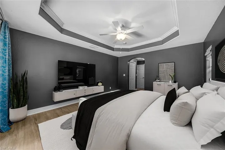 Bedroom with crown molding, arched walkways, wood finished floors, ceiling fan, and a raised ceiling