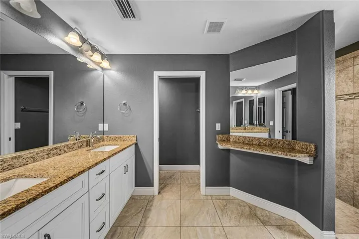 Bathroom featuring double vanity, a textured wall, and walk in shower