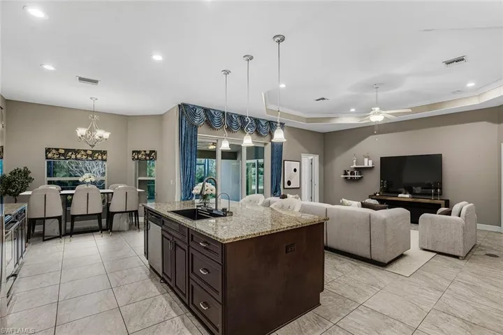 Kitchen featuring dark wood finish cabinets, suspended lighting, light stone counters, a center island with sink, and open floor plan