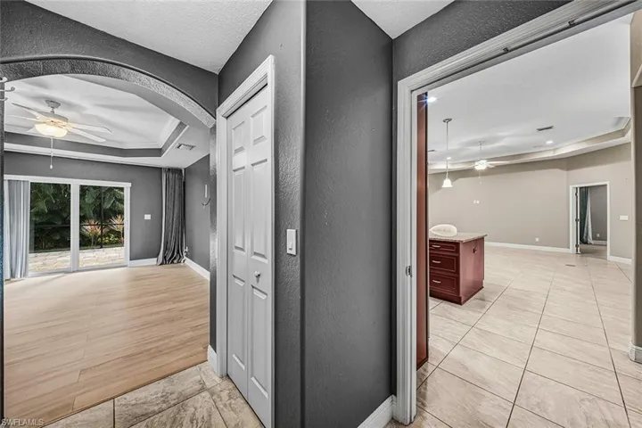 Corridor featuring a textured wall, a tray ceiling, a textured ceiling, light tile patterned floors, and arched walkways