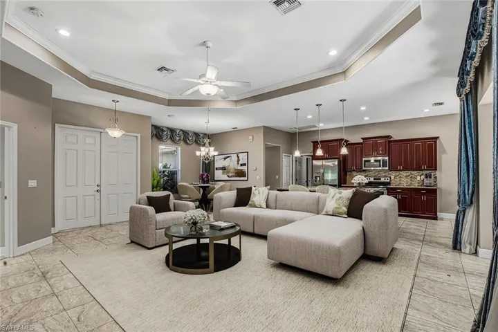 Living area with ceiling fan, crown molding, a tray ceiling, and a chandelier