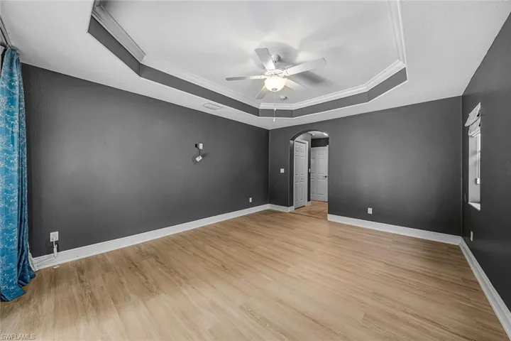 Spare room featuring arched walkways, crown molding, light wood-type flooring, ceiling fan, and a raised ceiling