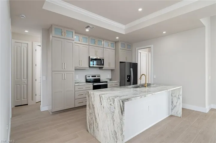 Kitchen with light stone countertops, sink, a tray ceiling, a center island with sink, and appliances with stainless steel finishes