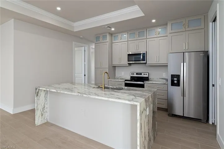 Kitchen featuring a center island with sink, a raised ceiling, sink, light stone counters, and stainless steel appliances