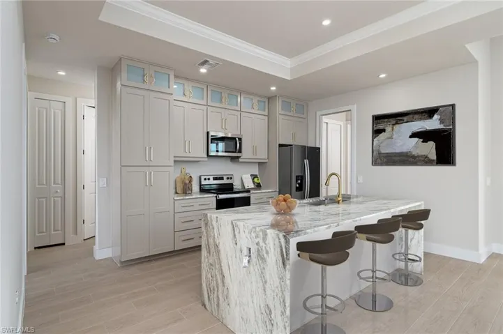 Kitchen with sink, stainless steel appliances, a raised ceiling, light stone counters, and a kitchen island with sink