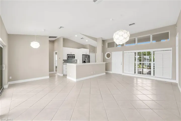 Unfurnished living room featuring high vaulted ceiling, light tile patterned floors, and a chandelier