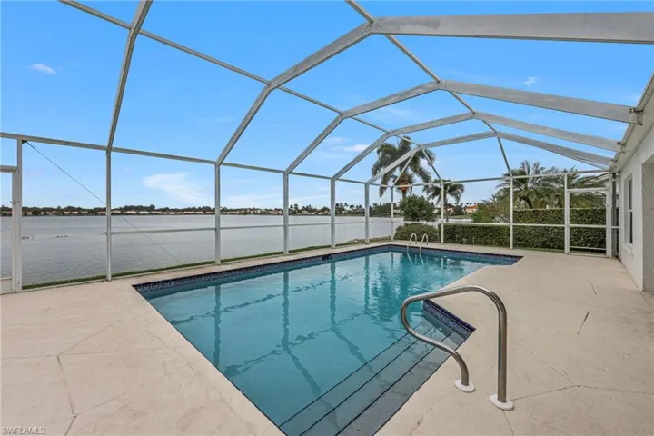 Outdoor pool with glass enclosure, a sunroom, a water view, and a patio area