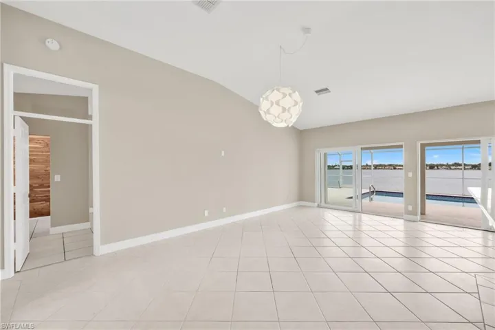Empty room featuring lofted ceiling, light tile patterned flooring, and a water view