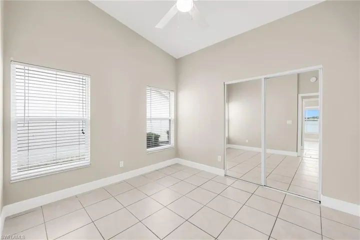 Unfurnished bedroom with a closet, ceiling fan, light tile patterned flooring, and high vaulted ceiling