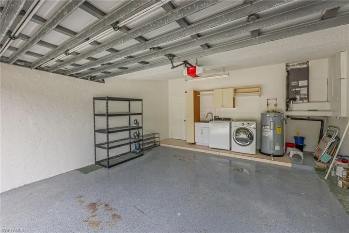 Garage with a textured wall, water heater, heating unit, independent washer and dryer, and a garage door opener
